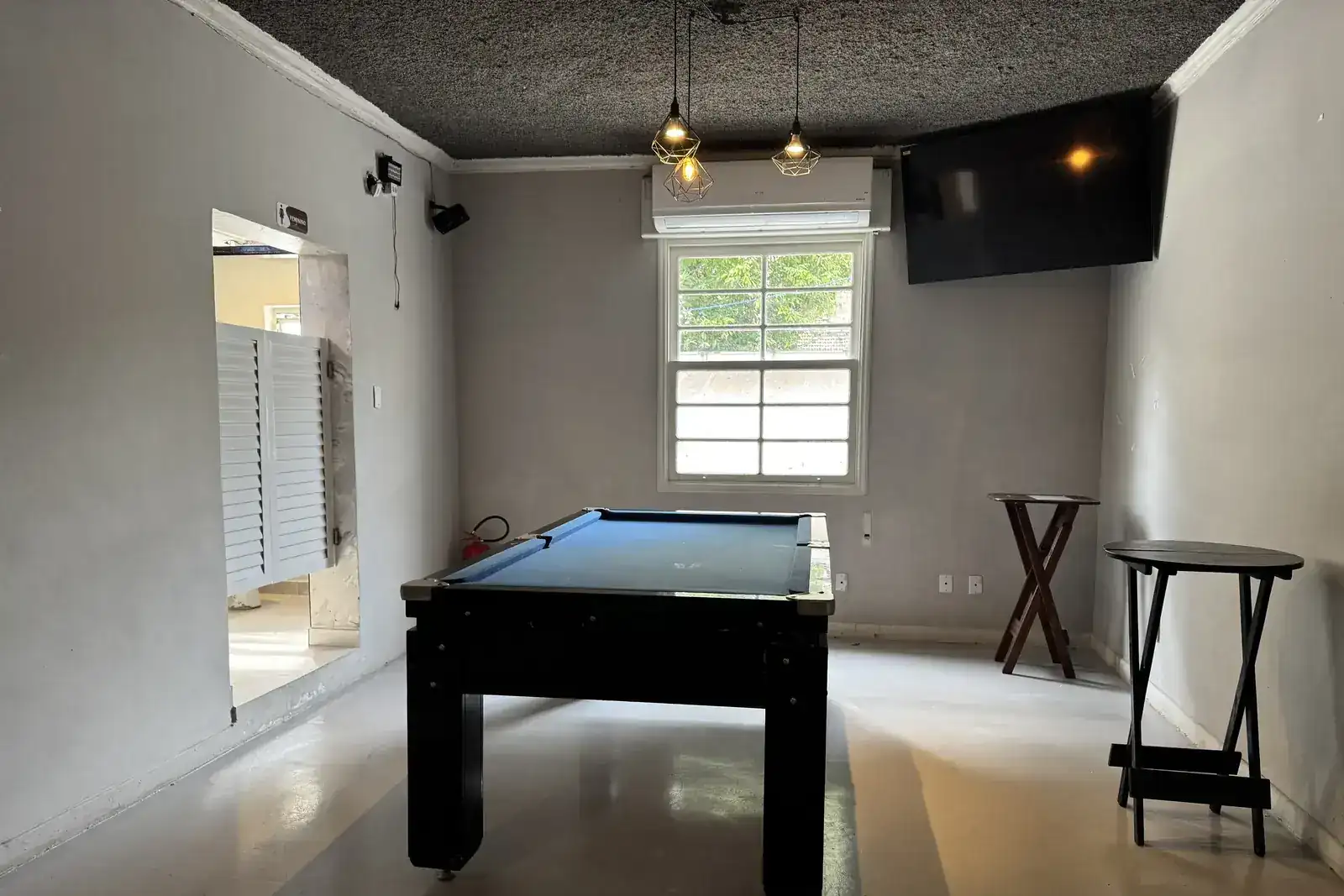 Sala de sinuca do Zora Bar com mesa profissional, TV e pendentes
