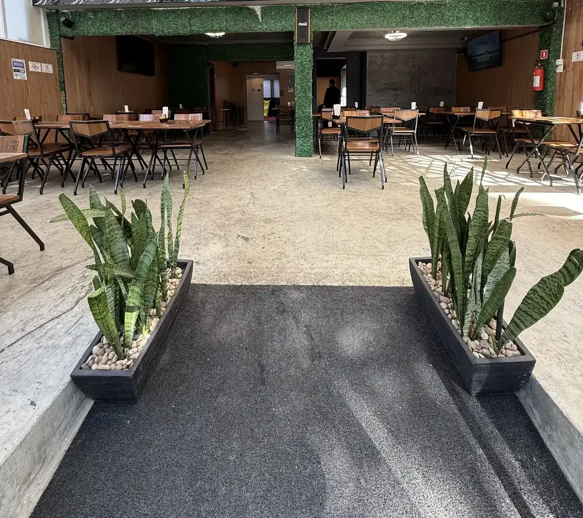 Salão principal do Zora Bar com mesas de madeira, jardim vertical e cobertura translúcida